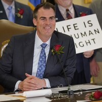 Kevin Stitt, une rose à la boutonnière, arbore un large sourire devant une pancarte disant : « La vie est un droit de la personne ».