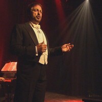Un homme chante devant une foule accompagné d'un pianiste