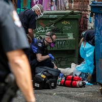 Des ambulanciers aident une personne allongée au sol dans une ruelle. 