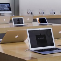 Plusieurs ordinateurs portables de la marque Apple sont disposés sur des tables. 