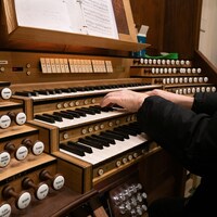 On voit des mains jouer sur le clavier d'un orgue, entourées par les boutons de contrôle.