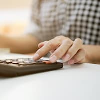 Gros plan sur la main d'une femme qui appuie sur une touche d'une calculatrice en faisant son budget.