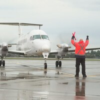 Un homme, vêtu de rouge aide un avion bi-moteur de la compagnie PAL Airlines à se stationner à l'aéroport de Charlottetown.