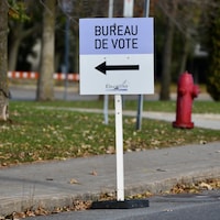 Une pancarte annonçant un bureau de vote, avec une borne-fontaine en arrière-plan.