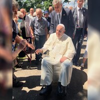 Assis dans son fauteuil roulant, le pape François serre des mains en souriant
