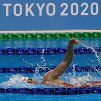 Une femme qui nage dans une piscine avec l'inscription TOKYO 2020 à l'arrière.