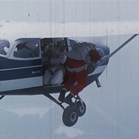 Un homme en combinaison avec un parachute au dos est agenouillé sur le rebord d'un avion.