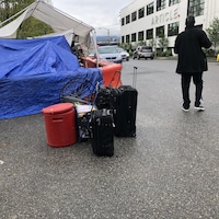 Quelques valises et d'autres contenants sont au sol, devant une tente en cours de démontage.