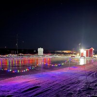 Une patinoire éclairée par la lumière d'une cabane et des lumières de Noël dans la prairie du Manitoba.