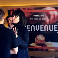 Pauline Larouche, directrice générale et fondatrice de l'événement culinaire Sherbrooke t'en bouche un coin, devant une grande affiche de l'événement. 