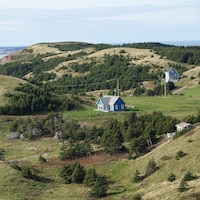 Quelques maisons éparses dans un paysage vallonné avec la mer en arrière-plan.