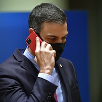 Pedro Sanchez tient un téléphone cellulaire rouge contre son oreille droite.