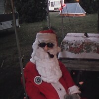 Un mannequin déguisé en père Noël est assis sous l'auvent d'une tente roulotte sur un terrain de camping.