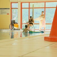 Une femme à mobilité réduite entre dans une piscine avec l'aide d'un lève-personne.
