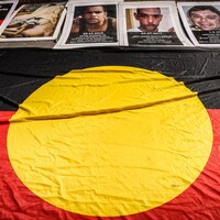 Des photos de personnes issues de Premières Nations d'Australie, mortes en détention, surplombent le drapeau aborigène.