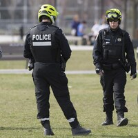 Deux policiers dans un parc près d'un homme portant un masque et posant le pied sur un ballon de soccer.