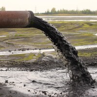 Un tuyau déverse de l'eau polluée sur un terrain vague.