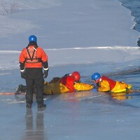 Deux pompiers couchés sur la glace tirent un troisième pompier qui fait la victime. 