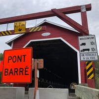 Des blocs de béton empêchent l'accès au pont couvert et un panneau de signalisation indique "pont barré".