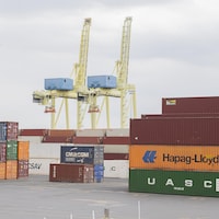 De grands conteneurs sont empilés dans une cour extérieure du port de Montréal. L'endroit est désert.