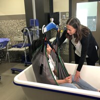 Une femme aide une autre femme à sortir d'une baignoire en utilisant un lève-personne.