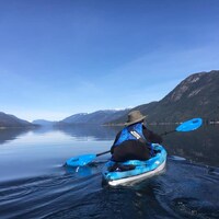 Une personne en kayak dans l'anse Sechelt, avec les montagnes en arrière plan et un ciel complètement dégagé