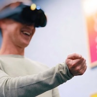 L'homme, tout sourire, tend le bras en portant un casque de réalité virtuelle sur sa tête. 