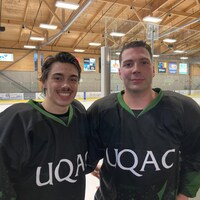 Deux jeunes hommes en uniforme de hockey devant une glace dans un aréna.