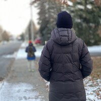 Une mère de dos regardant un garçon portant un sac à dos s'éloigner sur le trottoir