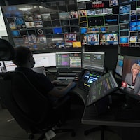 Un homme assis devant des consoles, des écrans d'ordinateurs et des écrans de télévision, dans la pénombre d'un studio.