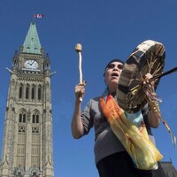 Une femme autochtone joue du tambourin devant l'édifice du parlement à Ottawa.