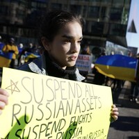 Une femme sur une place publique tient une pancarte jaune dénonçant la Russie.