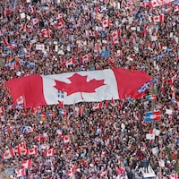 Un large drapeau canadien flotte au-dessus d'une foule.