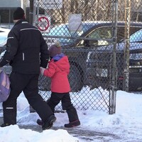Un homme tient une fillette par la main et transporte son sac d'école.