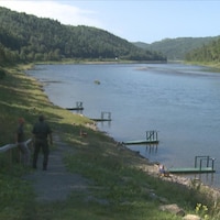 Deux hommes regardent la rivière Restigouche bordée de quais.
