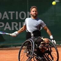 Un homme joue au tennis assis sur un fauteuil roulant. 