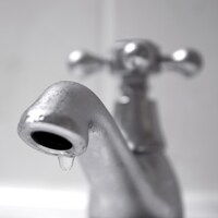 Une goutte d'eau suspendue à un robinet fermé.