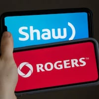 Une main tient deux téléphones arborant les logos de Shaw et de Rogers.