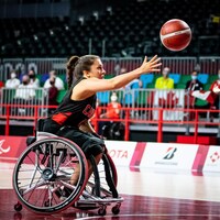 Une athlète en fauteuil roulant qui lance le ballon de basketball.