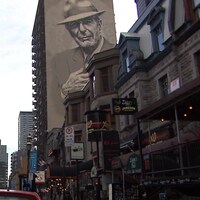 Des devantures de commerces rue Crescent, à Montréal, alors qu'on voit une murale de Leonard Cohen en arrière-plan.
