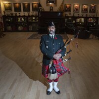 Un homme en uniforme pose dans le salon régimentaire du Black Watch à Montréal, sa cornemuse sous le bras.