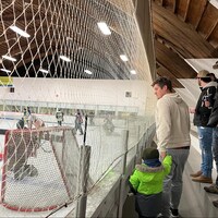 Un parent et son enfant regardent un match de hockey amateur à partir des estrades. 