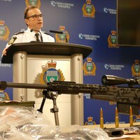 Danny Smyth devant un fusil muni d'une lunette, ainsi que plusieurs armes de poing.