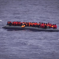 Une embarcation remplie de migrants flotte sur la mer.