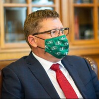 Scott Moe, en complet, dans son bureau, portant un masque aux couleurs des Roughriders (archives).