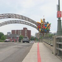 La ligne rouge est peinte sur le trottoir d'un pont. Une oeuvre composée de divers objets de plastique coloré est installée sur une arche du pont.