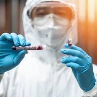 Un scientifique tient une seringue et une éprouvette sur laquelle il est écrit "COVID-19".