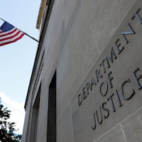 L'entrée du siège du département de la Justice des États-Unis, dont la façade indique « Département de la Justice » et est ornée d'un drapeau américain.