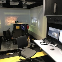 Un bureau avec des écrans d'ordinateur est placé dans un conteneur où on trouve également un simulateur d'équipement minier avec écran géant.