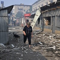 Une femme enjambe de débris qui jonchent le sol dans une rue. Les vitres des commerces situés à proximité ont toutes volé en éclats. 